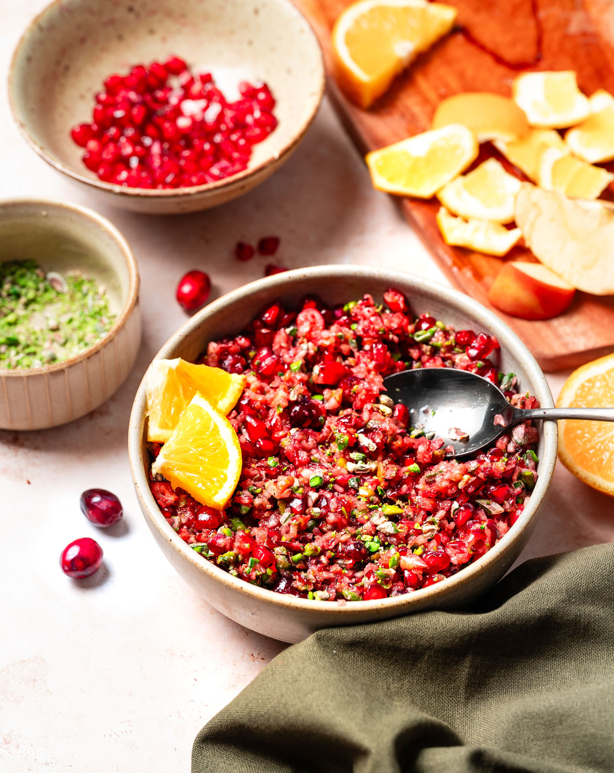 Bowl of homemade cranberry relish on table with cutting board and orange peels.