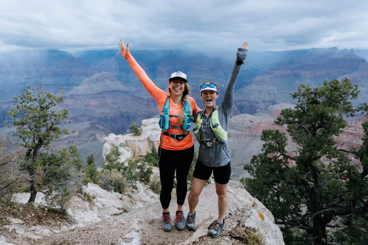 Two women standing on the rim of the Grand Canyon with their arms in the air.