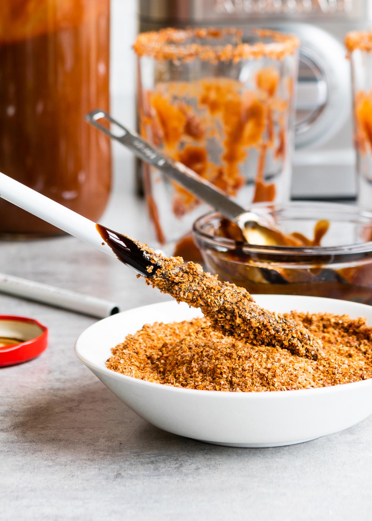 A metal straw being dipped into a white bowl of Tahin seasoning.