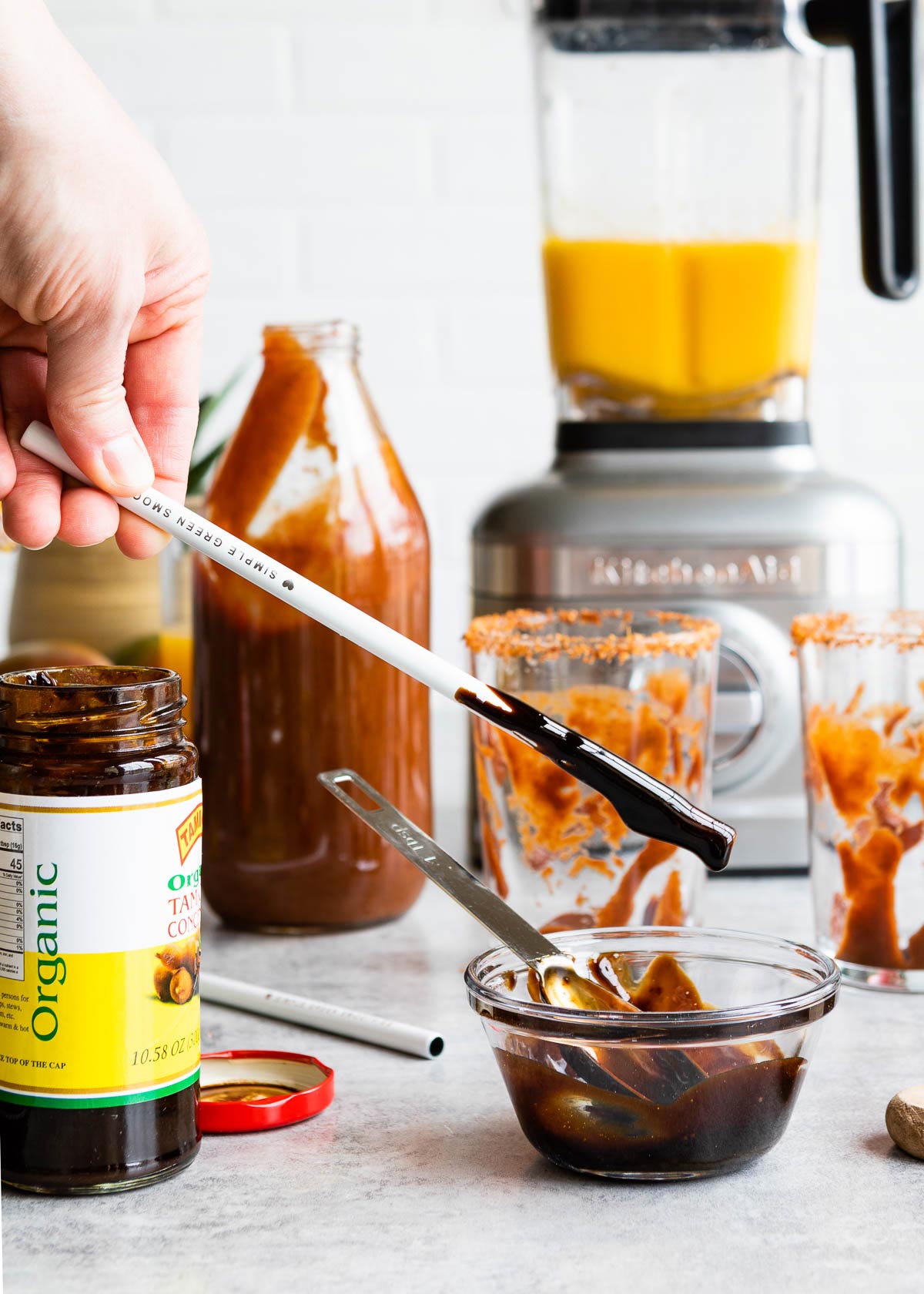 A metal straw being dipped into a glass bowl filled with tamarind concentrate and date syrup.