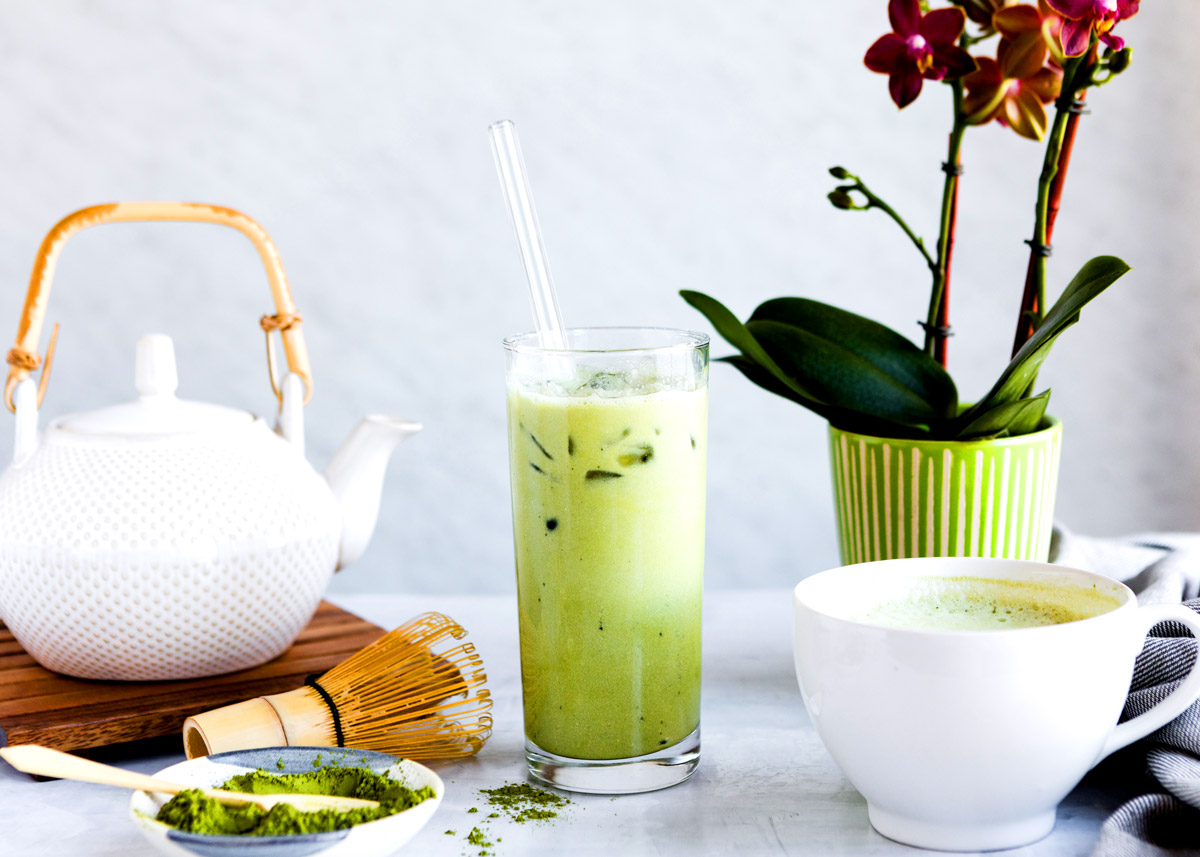 iced matcha latte next to a mug with hot matcha latte.