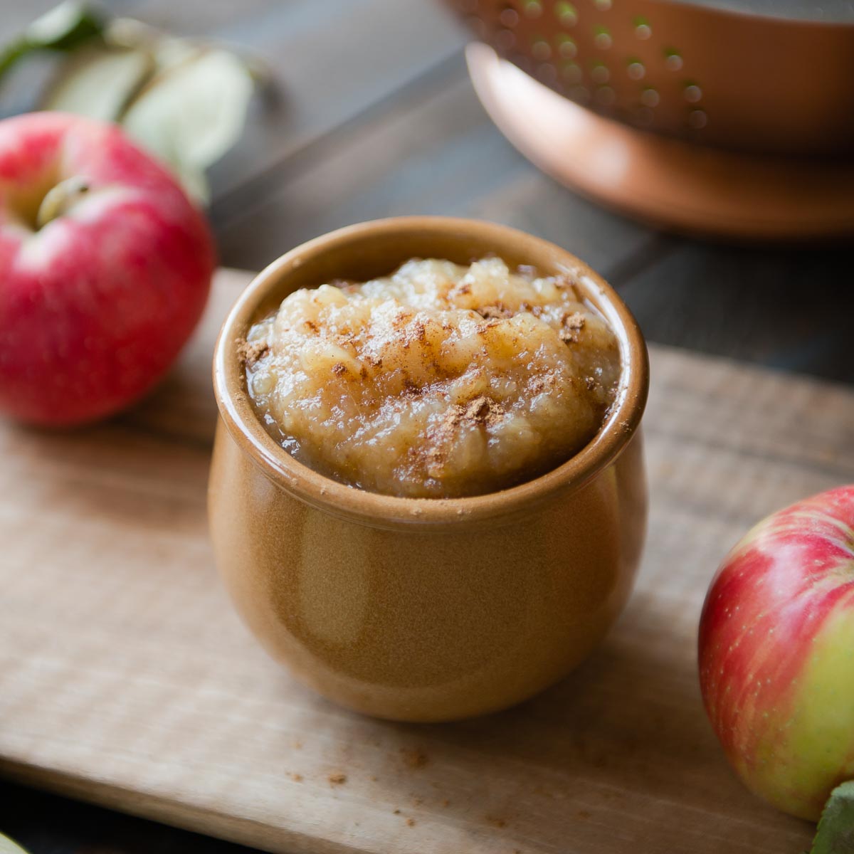 brown ceramic bowl full of slow cooker applesauce topped with cinnamon sitting on a wooden cutting board.